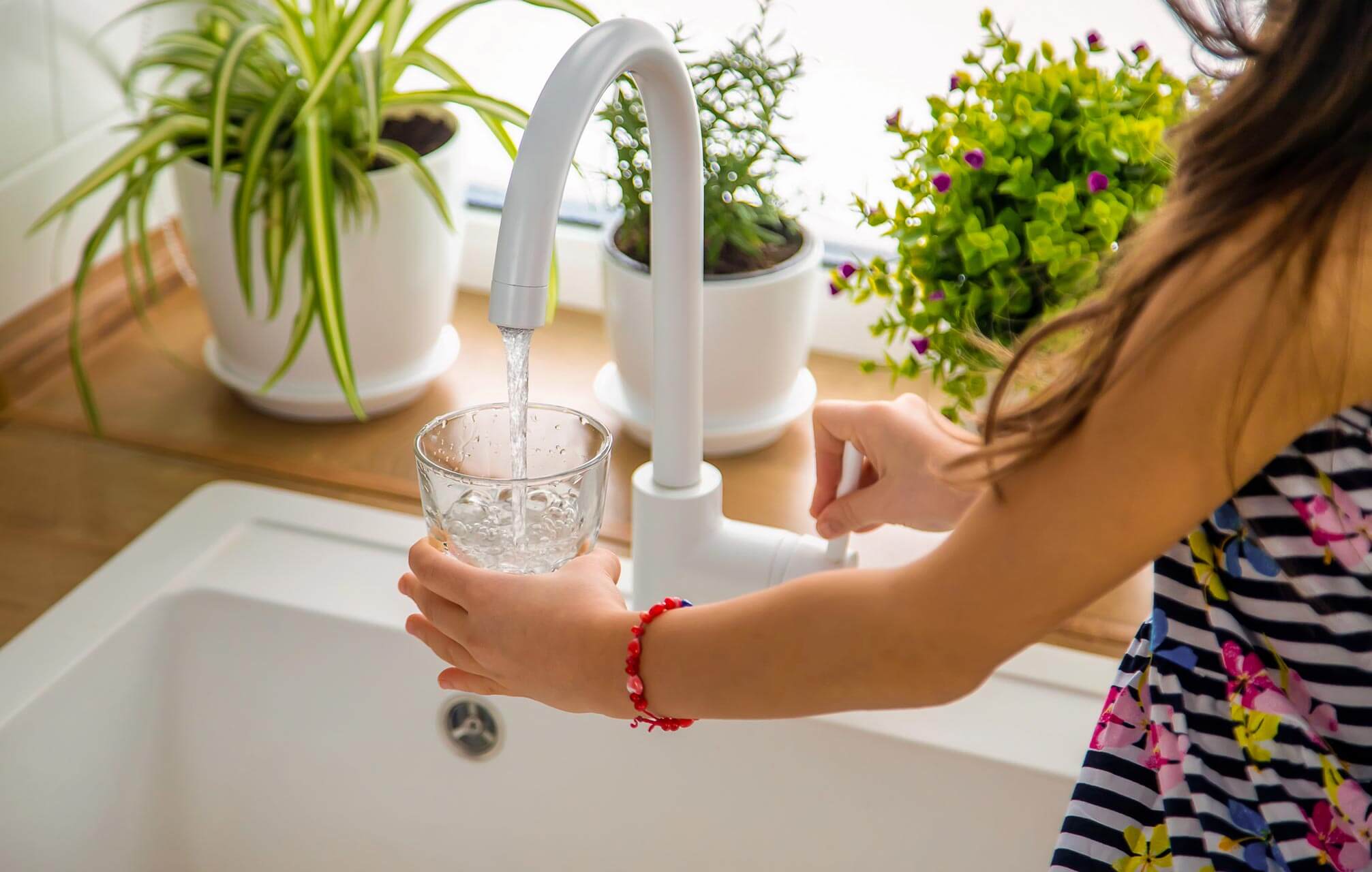 Photo of a woman filling up a glass of water from a sink tap - Carolina Heating Service Inc. Photo of a woman filling up a glass of water from a sink tap