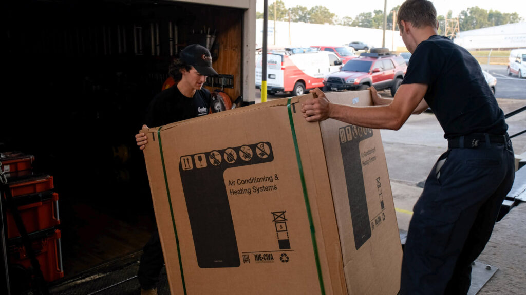 Two Carolina Heating Service technicians loading an air conditioning unit onto a truck - Carolina Heating Service Inc. Two Carolina Heating Service technicians loading an air conditioning unit onto a truck